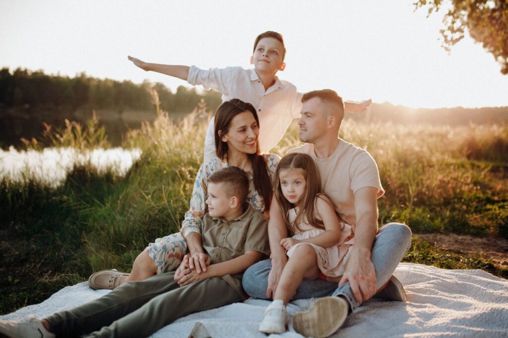 A family of five enjoying a serene picnic in a sunlit meadow during sunset.